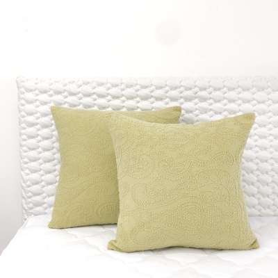 Duas almofadas verdes texturizadas numa cama com cabeceira branca e colcha branca