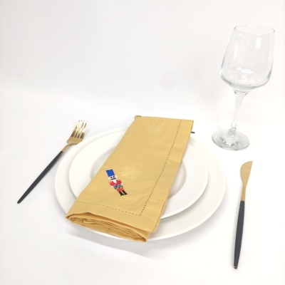 Conjunto de mesa com pratos brancos, guardanapo amarelo com bordado, talheres preto e dourado, copo de vinho transparente.