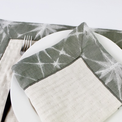 Jogo americano e guardanapo em tecido com padrão tie-dye cinza esverdeado e branco sobre prato branco.