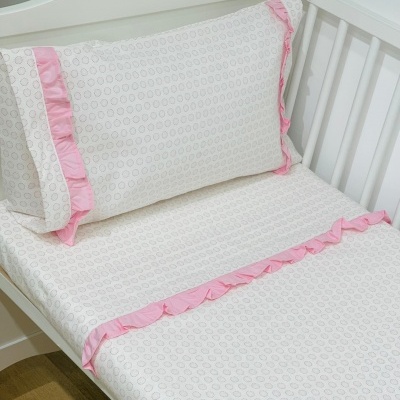 Cama de criança branca com roupa de cama branca com folho rosa