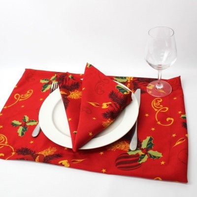 Conjunto de mesa natalício com toalha e naparela vermelha estampada, prato branco, talheres e copo de vidro.