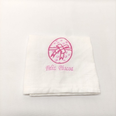 Toalha branca com bordado rosa de ovo e texto Feliz Páscoa