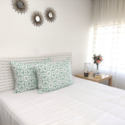 Quarto com cama branca, almofadas verdes florais, espelhos redondos e mesa de cabeceira com flores