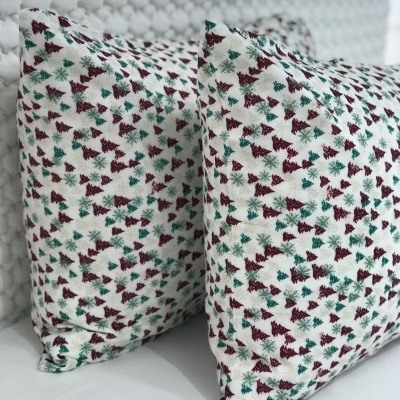 Duas almofadas com padrão de pinheiros verdes e bordô sobre fundo branco colocadas numa superfície branca