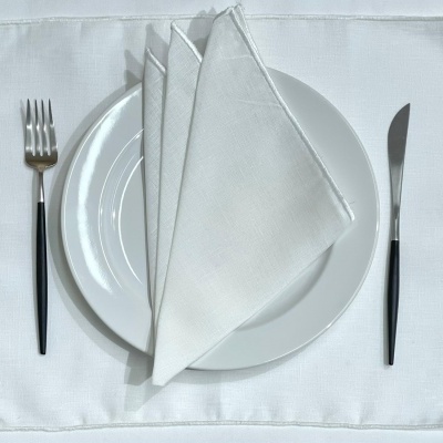 Conjunto de jantar com prato branco, guardanapo dobrado, garfo e faca com cabos pretos num lugar americano branco