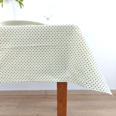 Toalha de mesa branca com padrão de losangos verdes e vermelhos sobre mesa de madeira clara