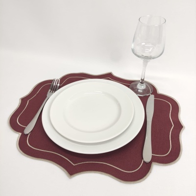 Pratos brancos, talheres, copo de vinho sobre suporte de tecido bordeaux
