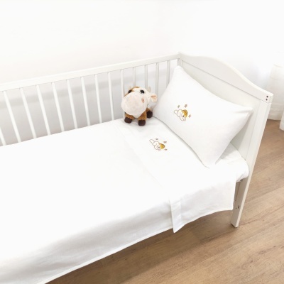 Cama de bebé branca com roupa de cama branca decorada com ursinho bordado e peluche de vaca