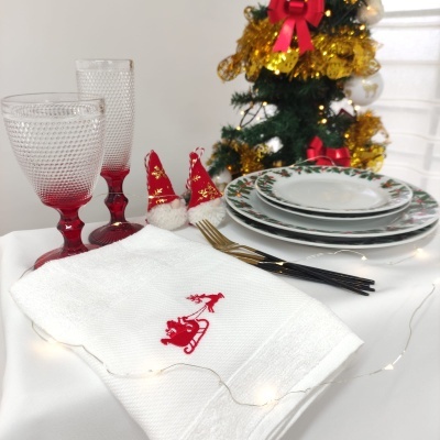 Conjunto de louça natalina, copos vermelhos texturizados, talheres dourados, panos bordados e árvore de Natal ao fundo