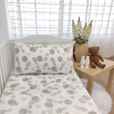 Cama de bebé com roupa de cama estampada, mesa ao lado com ursos de pelúcia e flores
