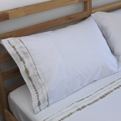 Travesseiros com fronhas brancas e bordas com padrão castanho em cama de madeira clara