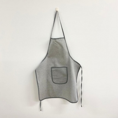 Avental cinzento xadrez com bolso frontal pendurado numa parede branca