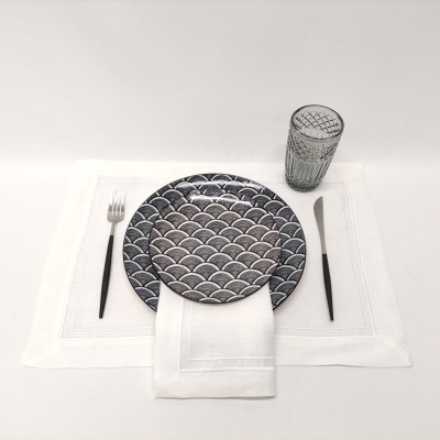 Jogo de jantar com pratos cinzentos, copo de vidro texturizado, talheres pretos e guardanapo branco