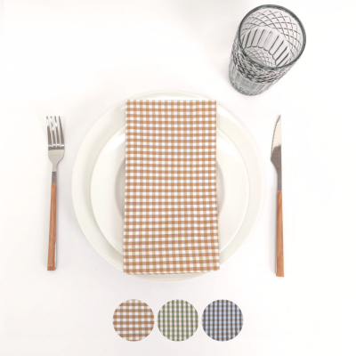 Mesa posta com pratos brancos, guardanapo xadrez castanho, talheres com cabo de madeira e copo transparente