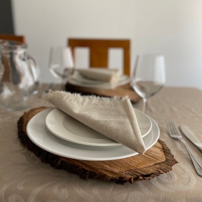Conjunto de jantar com pratos brancos, guardanapo bege e base de madeira sobre toalha texturada