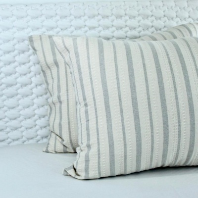 Três almofadas riscas cinza e bege sobre manta branca de malha.