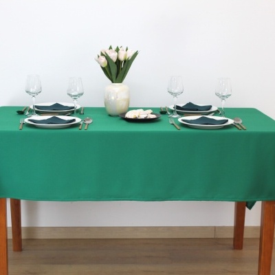 Mesa de jantar com toalha verde, pratos, copos, talheres e jarro com flores brancas