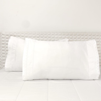 Três almofadas brancas sobre cama com colcha branca e cabeceira texturizada