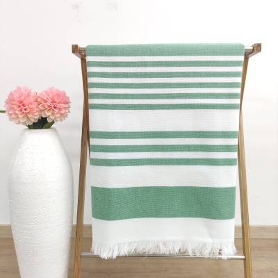 Toalha de riscas verdes e brancas pendurada em suporte de madeira ao lado de vaso branco com flores cor de rosa
