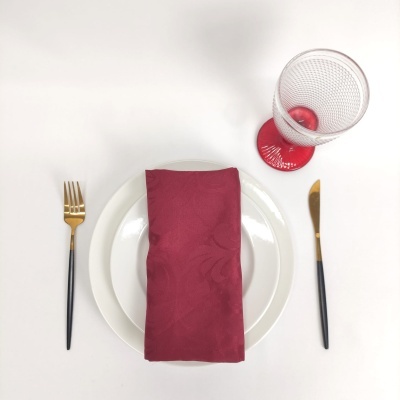 Mesa posta com prato branco, guardanapo vermelho, talheres com cabo preto e dourado e copo transparente com base vermelha