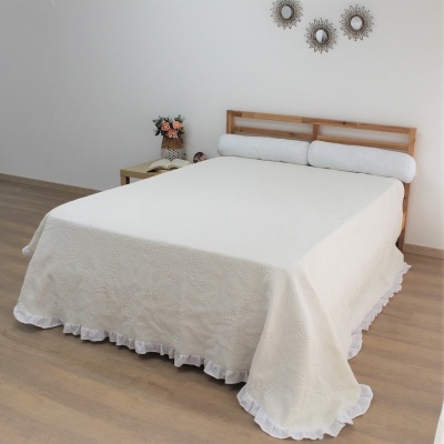 Cama de madeira com colcha creme e travesseiros cilíndricos, mesa com flores e espelhos redondos na parede