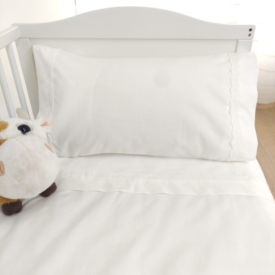 Conjunto branco de roupa de cama bordada num berço com brinquedo de pelúcia