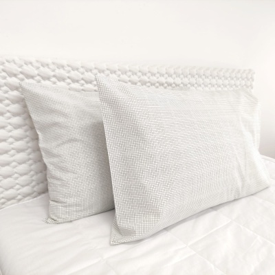 Duas almofadas brancas com padrão de quadrados pequenas sobre cama branca com cabeceira texturizada.