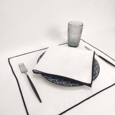 Conjunto de mesa com guardanapo branco, prato azul escuro com padrão, copo transparente, faca e garfo com cabos pretos