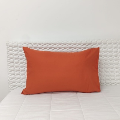 Almofada rectangular laranja numa cama com colcha e cabeceira brancas
