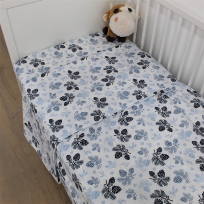 Cama de bebé com roupa de cama branca com padrão floral azul e preto e peluche de vaca