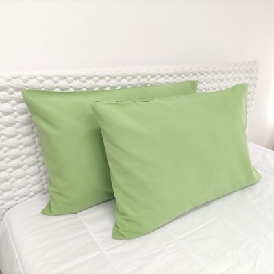 Duas almofadas verdes retangulares em cama branca com cabeceira branca texturizada