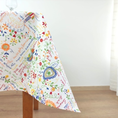 Toalha de mesa colorida com padrão floral e texto, sobre mesa de madeira em ambiente interior claro