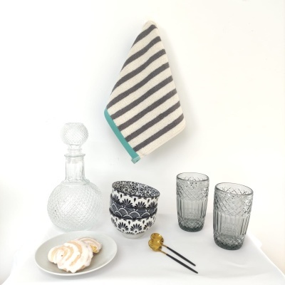 Conjunto de mesa com garrafa de vidro, copos, tigelas, prato com pastelaria, guardanapo às riscas e utensílios dourados