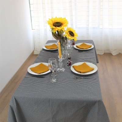 Mesa de jantar com toalha xadrez, pratos brancos, guardanapos amarelos e girassóis em vaso