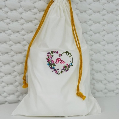 Saco de tecido branco com cordão amarelo e bordado floral colorido