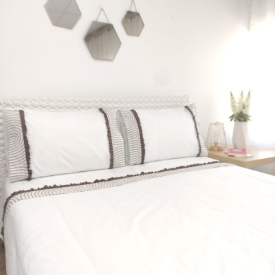Cama com roupa de cama branca com detalhes em cinza e castanho em quarto moderno branco com espelhos hexagonais e mesa de cabeceira