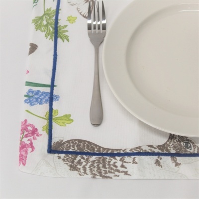 Toalha branca com padrões de flores e aves, garfo e prato branco