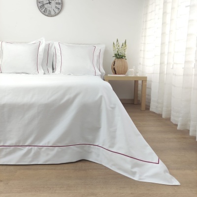 Roupa de cama branca com linhas vermelhas numa cama de casal em quarto com decoração clara e minimalista