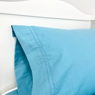 Almofada azul clara com costura decorativa numa cama branca