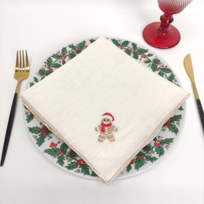 Conjunto de jantar natalício com prato decorado, guardanapo com boneco de gengibre, talheres dourados e copo vermelho.