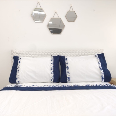 Conjunto de cama branco e azul com franjas florais e três espelhos hexagonais na parede.
