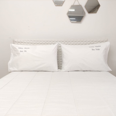 Cama com almofadas brancas bordadas e cabeceira cinzenta trançada