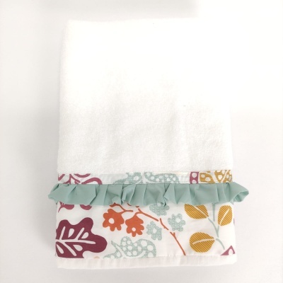 Toalha branca com barra decorativa floral colorida e franzido verde claro.