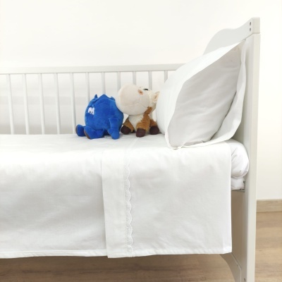 Berço branco com roupa de cama branca e dois peluches sobre o colchão