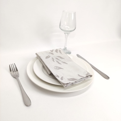 Jogo de jantar com pratos brancos, talheres em metal, guardanapo cinza com padrão de folhas e taça de vidro
