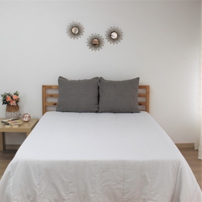 Cama de solteiro com colcha branca e duas almofadas cinzentas com padrão texturizado