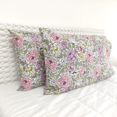 Almofadões com capas florais em cama branca com cabeceira texturizada