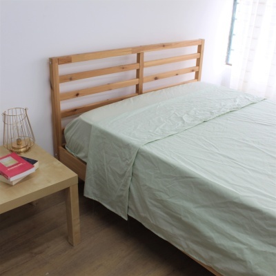 Cama de casal com cabeceira de madeira clara e lençol verde