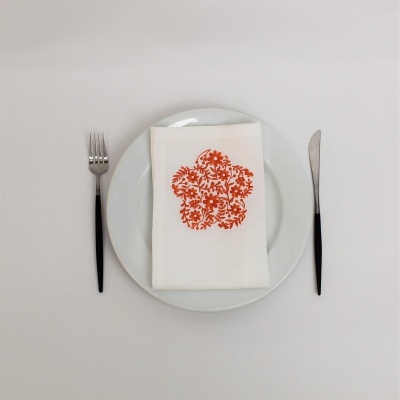 Prato branco com guardanapo branco decorado e talheres com cabos pretos num fundo branco.