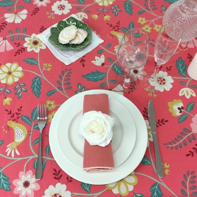 Mesa posta com toalha floral rosa, prato e guardanapo com flor, talheres e copos